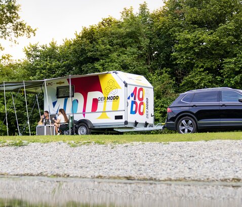 Camping Humbaur MODO | © Humbaur GmbH MODO kampeerwagen met kampeeraccessoires op een weiland aan het meer. | © Humbaur GmbH