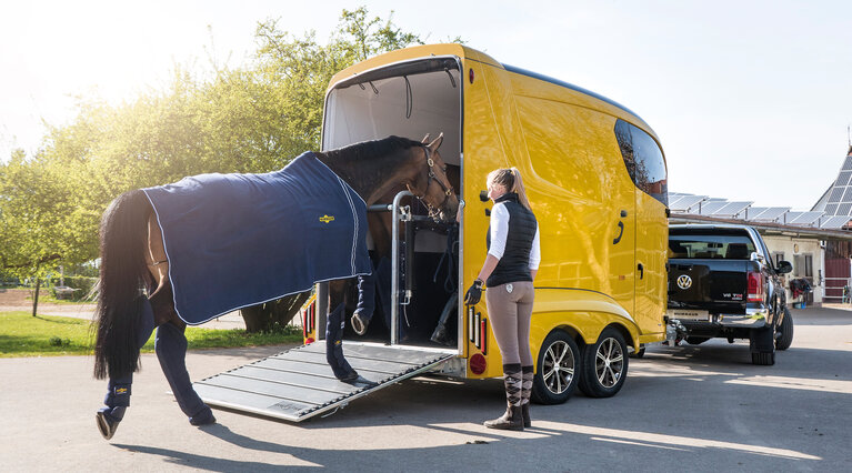 Eine Reiterin führt ihr Pferd in einen gelben Humbaur Pferdanhänger Modell Maximus. | © Humbaur GmbH