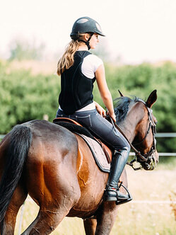 De dos, on voit une cavalière assise sur un cheval brun. 