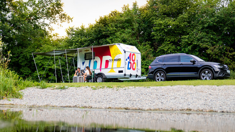 Multifunktionsanhänger MODO mit Campingzubehör steht auf Wiese am See. | © Humbaur GmbH