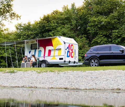 Campinganhänger MODO mit Campingzubehör steht auf Wiese am See. | © Humbaur GmbH