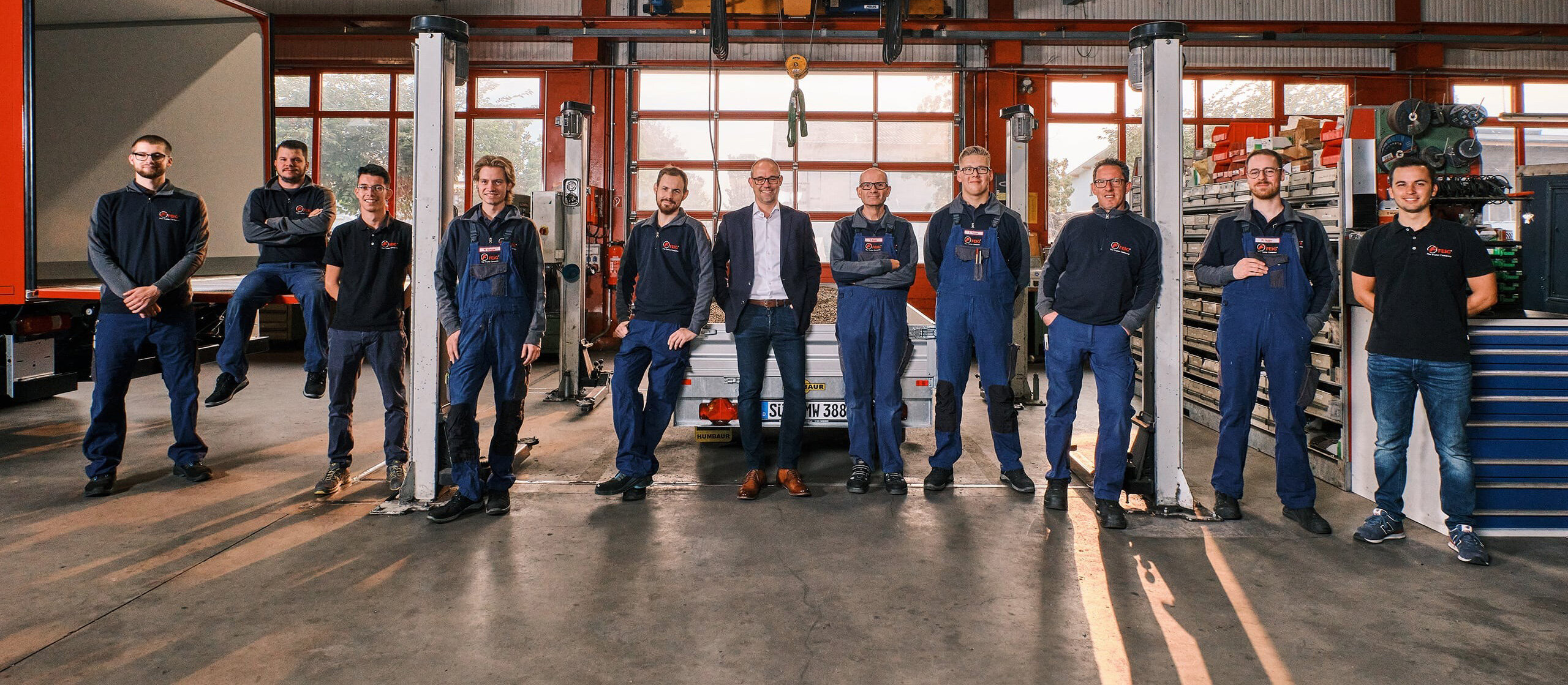 Mitarbeiter der Firma Feig stehen nebeneinander in der Werkstatt und lächeln in die Kamera.